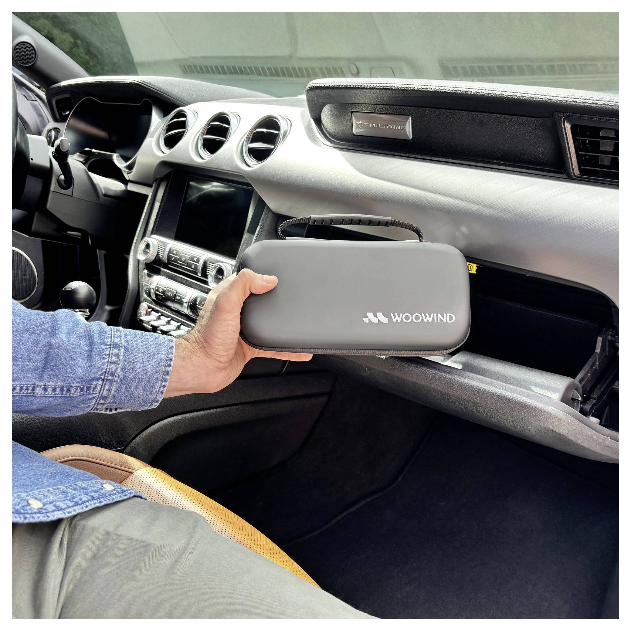 Ruka držící šedý WOOWIND zip obal uvnitř interiéru automobilu s otevřenou rukavičkou.