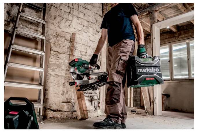Osoba v ochranném vybavení nese pouzdro na elektrické nářadí značky "Metabo" a nástroj v nedokončené místnosti se žebříkem a odkrytými cihlami.