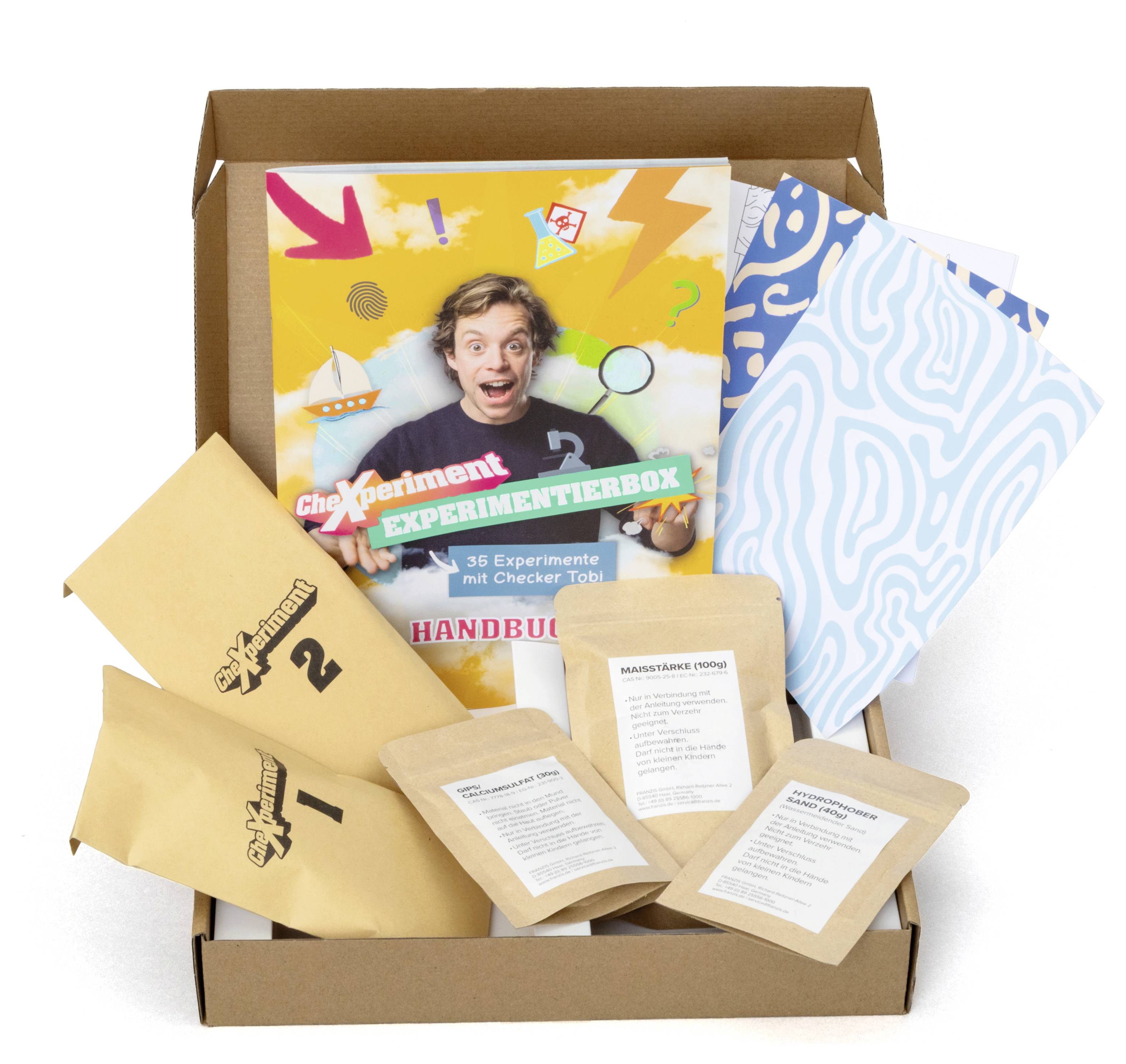Sada "Experimentier Box" obsahující experimentální pomůcky, manuál s osobou nadšeně demonstrující a různé označené balíčky.
