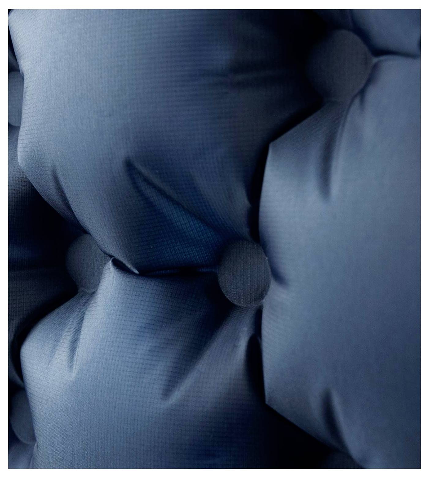 Detailní záběr na modré čalounené ploše s prošíváním a knoflíky, které vytvářejí strukturovaný vzor.