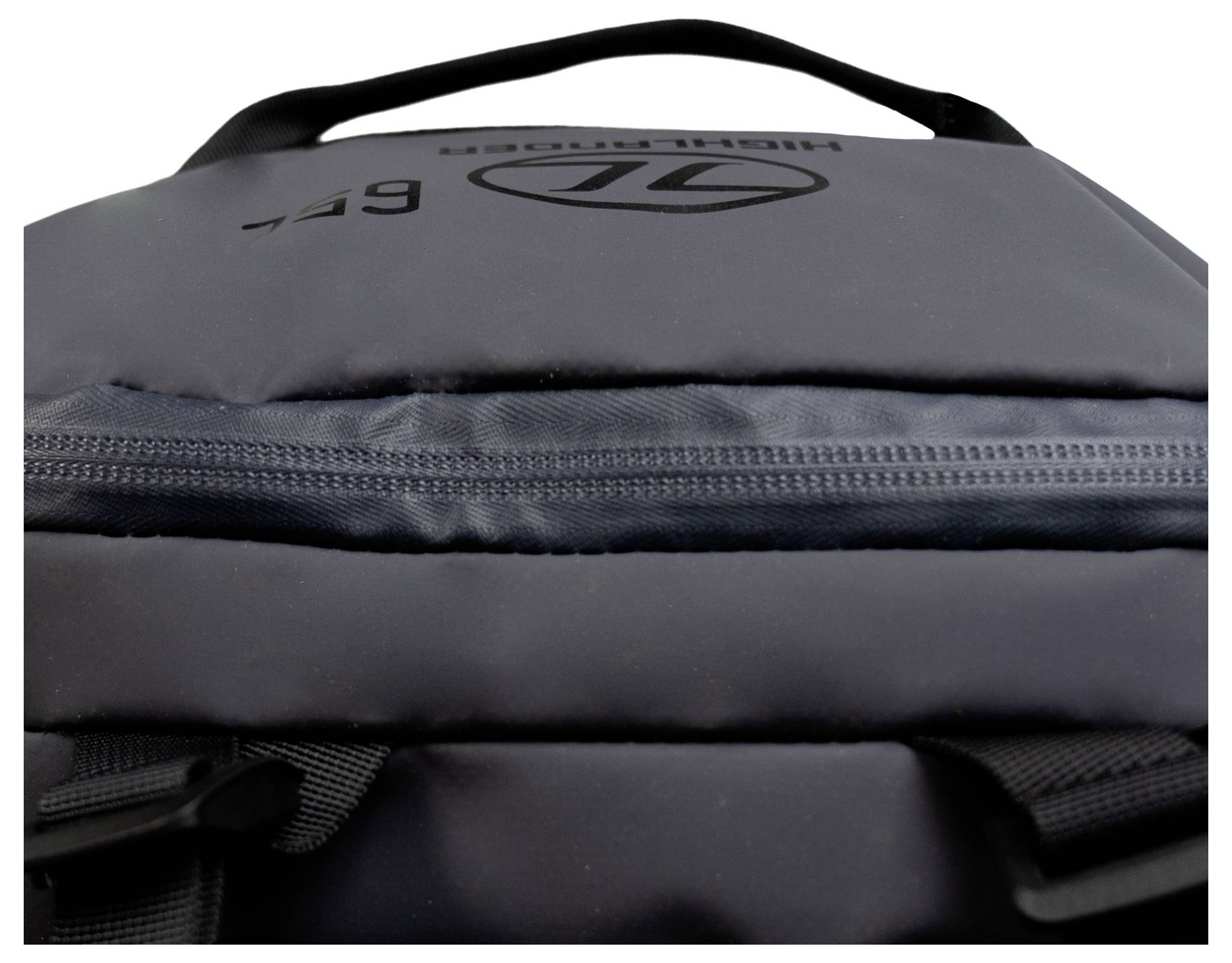 Detailní snímek černého batohu zobrazující zip a část rukojeti s viditelným logem na tkanině.