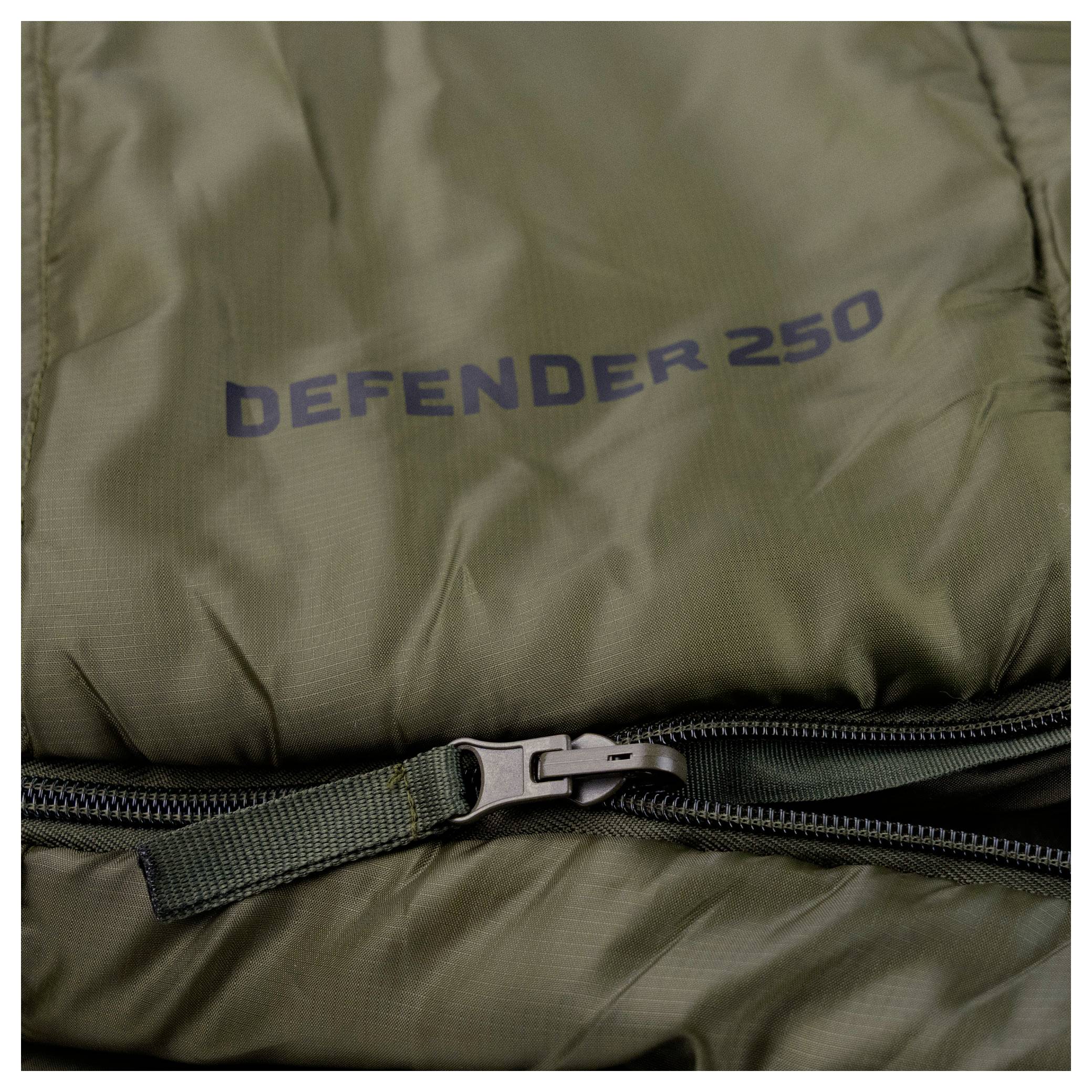 Detailní pohled na zelený spacák se zipem částečně otevřeným. Na tkanině nad zipem je vytisknout text "DEFENDER 250".