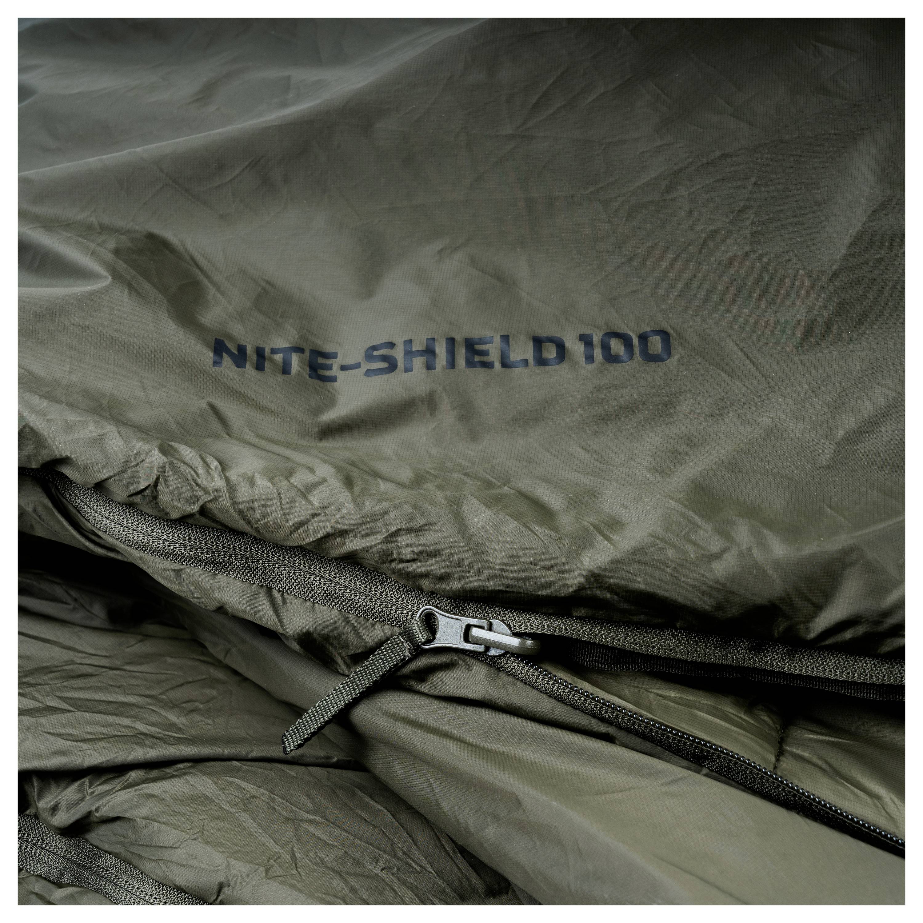 Spací pytel z tmavě zelené látky se zipem a textem "NITE-SHIELD 100" vytištěným na něm.