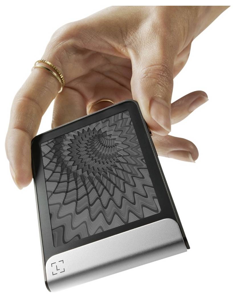 Ruka držící kompaktní digitální zařízení s černo-bílým geometrickým vzorem na obrazovce.