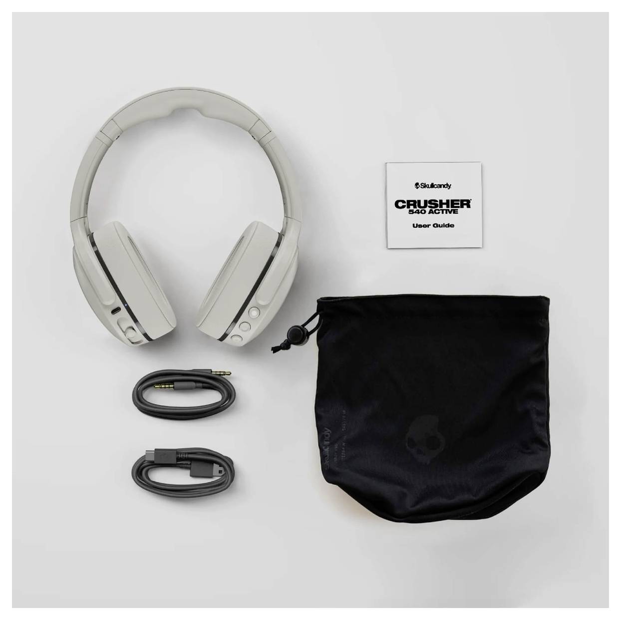 Bílá náhlavní sluchátka s uživatelskou příručkou, černým pouzdrem, audio kabelem a USB nabíjecím kabelem na šedém pozadí.