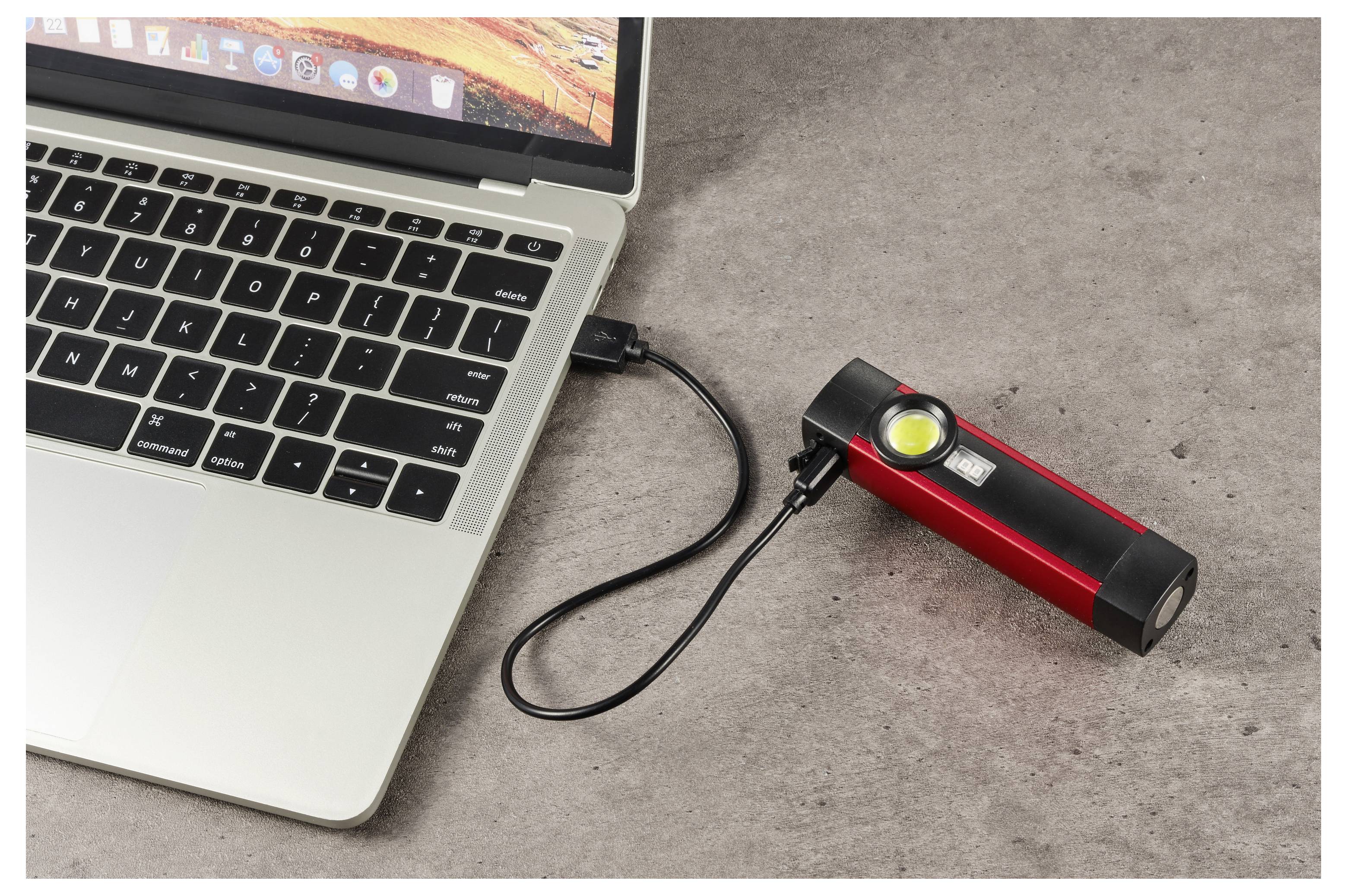Laptop připojený USB kabelem k červené přenosné powerbance s rozsvíceným indikátorem na pracovní ploše.