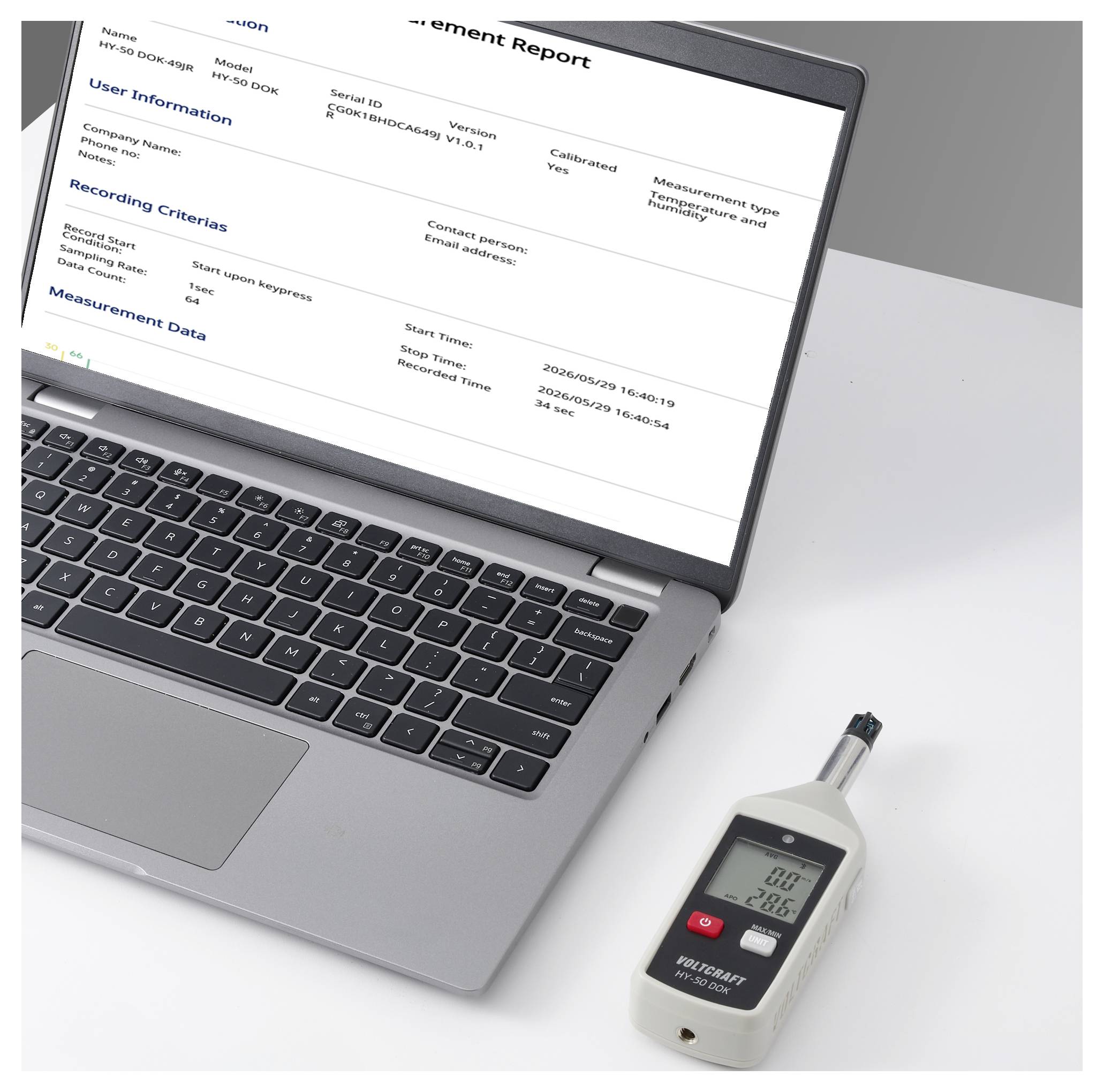 Laptop zobrazující zprávu o měření vedle ručního teploměru/vlhkoměru na stole, což naznačuje sběr a analýzu údajů o životním prostředí.