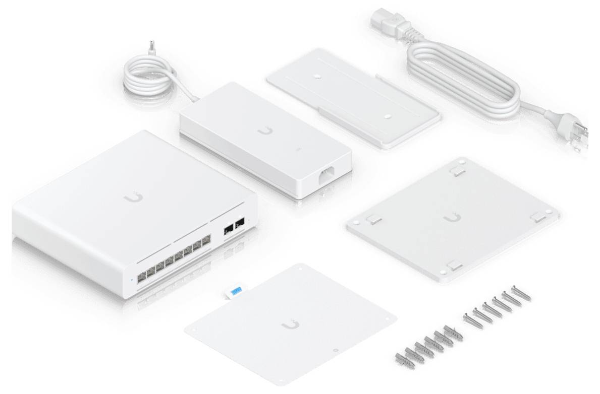 Součásti 'Ubiquiti UniFi Security Gateway' včetně brány, napájecího kabelu, upevňovacích držáků a šroubů, rozložené na bílém pozadí.