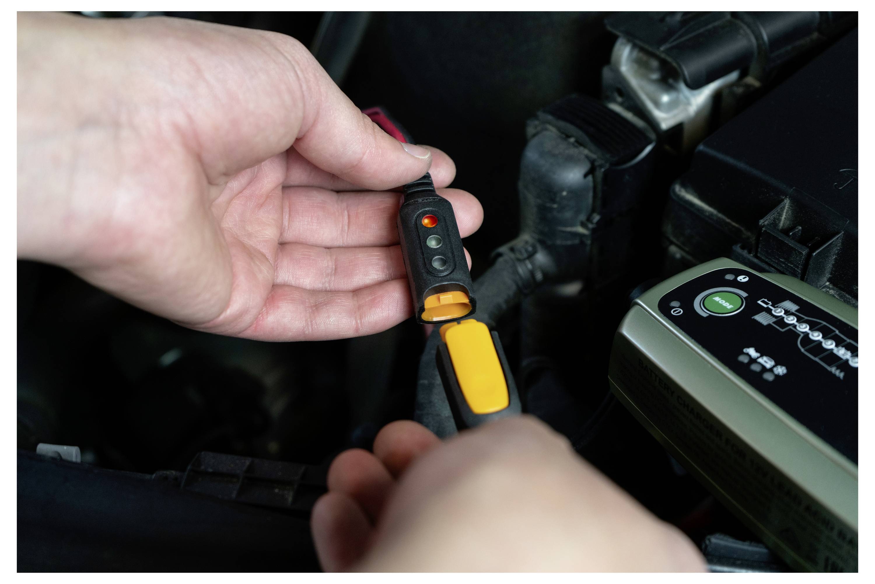 Osoba používající tester napětí v prostoru motorového prostoru automobilu k ověření elektrických spojů.