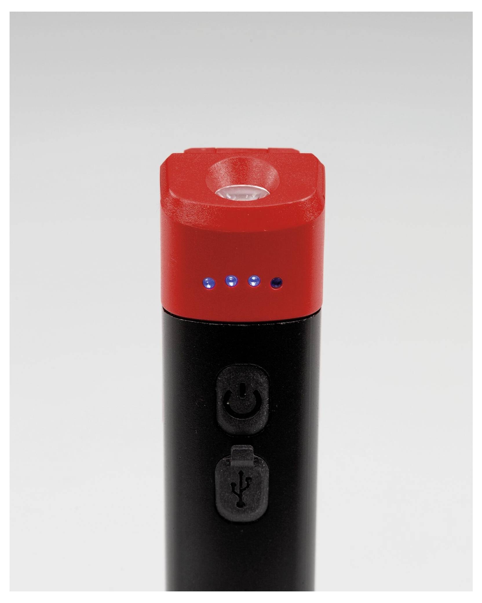 Černé a červené elektronické zařízení s LED indikátory a tlačítky napájení a USB, pravděpodobně powerbanka nebo podobný gadget, na neutrálním pozadí.