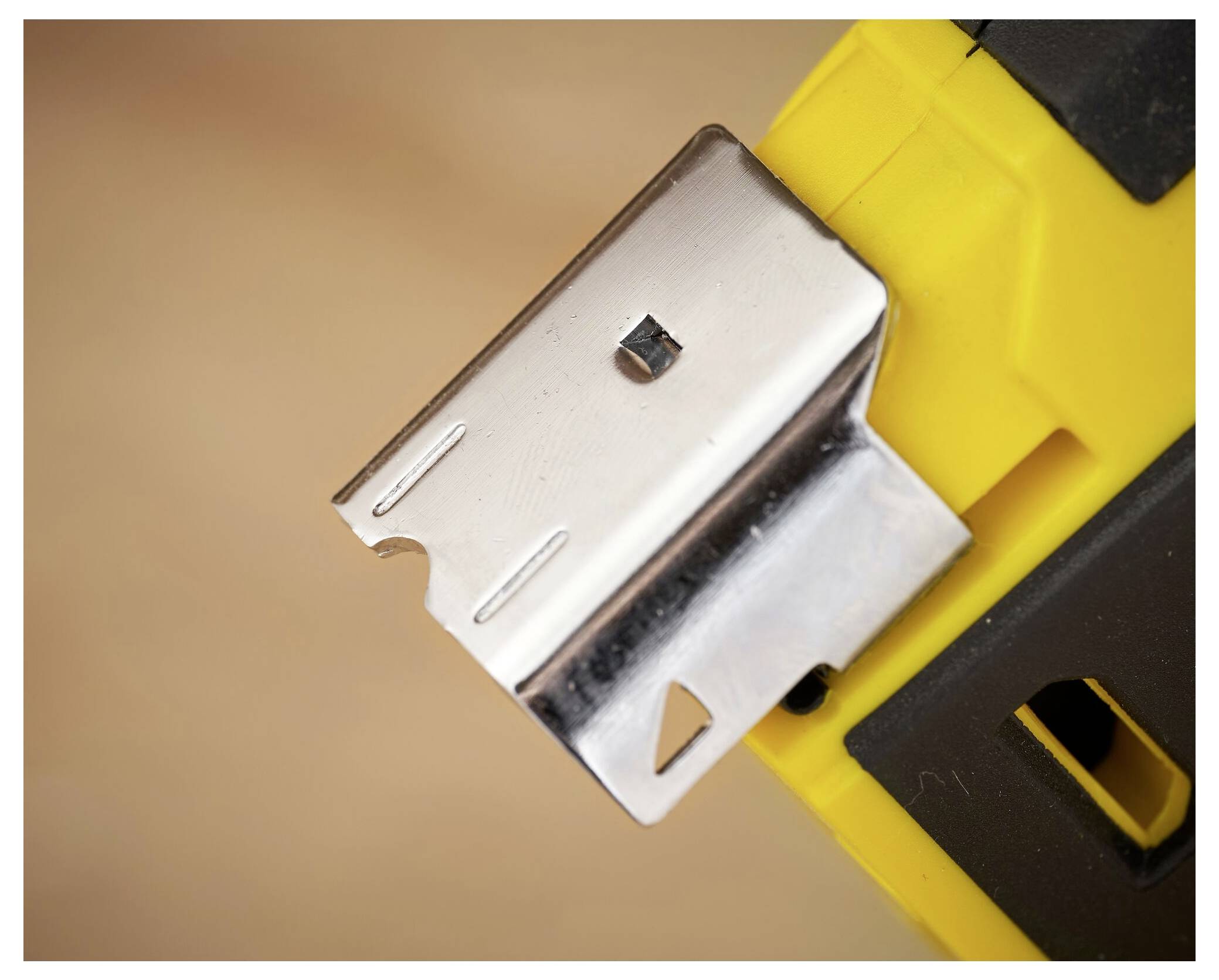 Detailní záběr na kovovou hlavu sponkovacího pistoletu se žlutou rukojetí, zobrazující nástroj používaný k upevňování materiálů ve stavebnictví nebo při ruční práci.