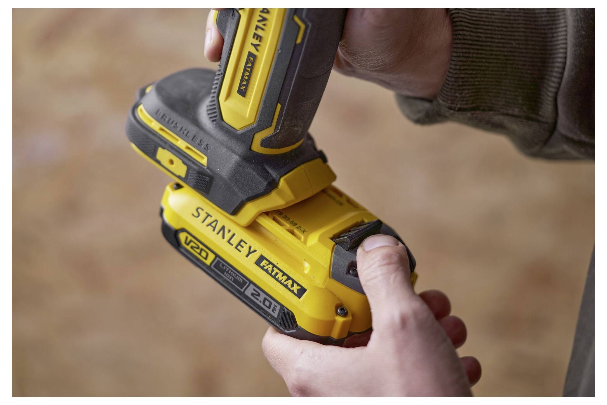 Osoba připojuje žlutou baterii "Stanley FATMAX V20 2.0Ah" na spodní stranu odpovídajícího žlutého elektrickéhonástroje v detailním záběru.