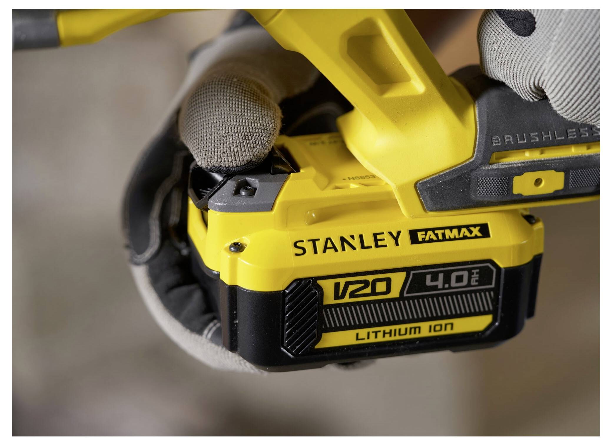 Osoba v rukavicích drží žlutou baterii Stanley Fatmax V20 4.0Ah s lithium-ionovou technologií a zobrazuje značku a kapacitu.