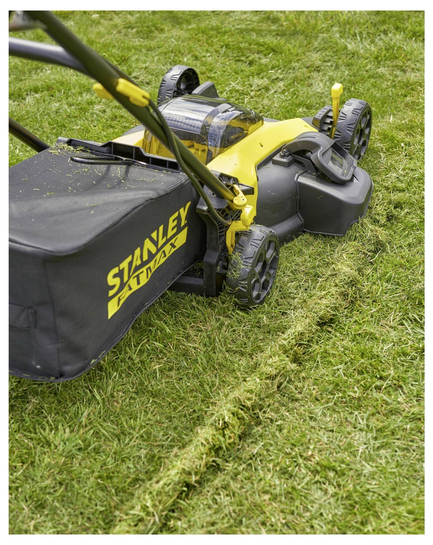 Žlutá sekačka na trávu střihající trávu a zanechávající úhlednou cestu na trávníku. Sekačka má na tašce na trávu značku "Stanley Fatmax".