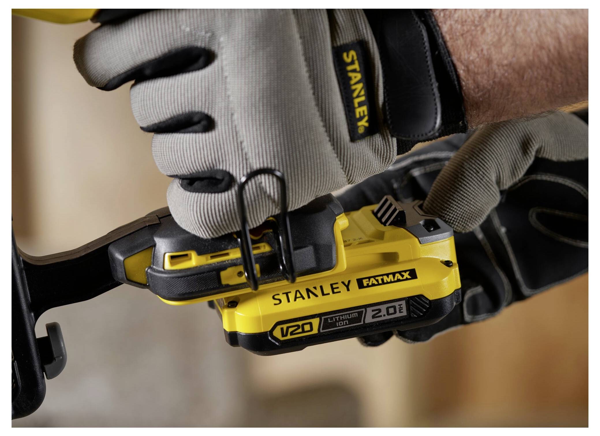 Rukavicí opatřená ruka ovládá žlutý Stanley Fatmax V20 elektrickýnářadí, což naznačuje použití při stavebních nebo opravářských pracích.