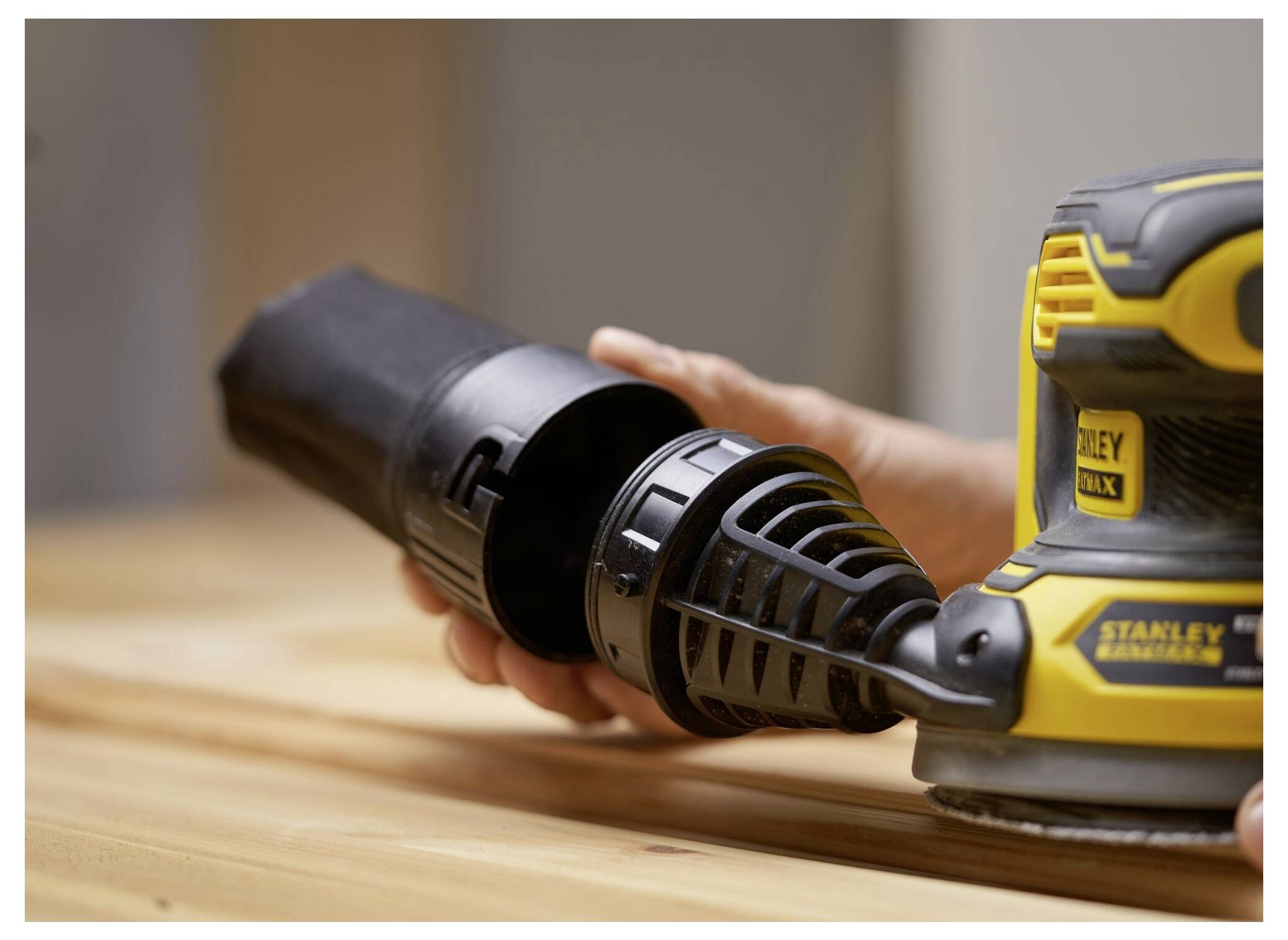 Osoba skládá žluto-černou brusku na dřevěné podložce a soustředí se na připevnění nádoby na sběr prachu.