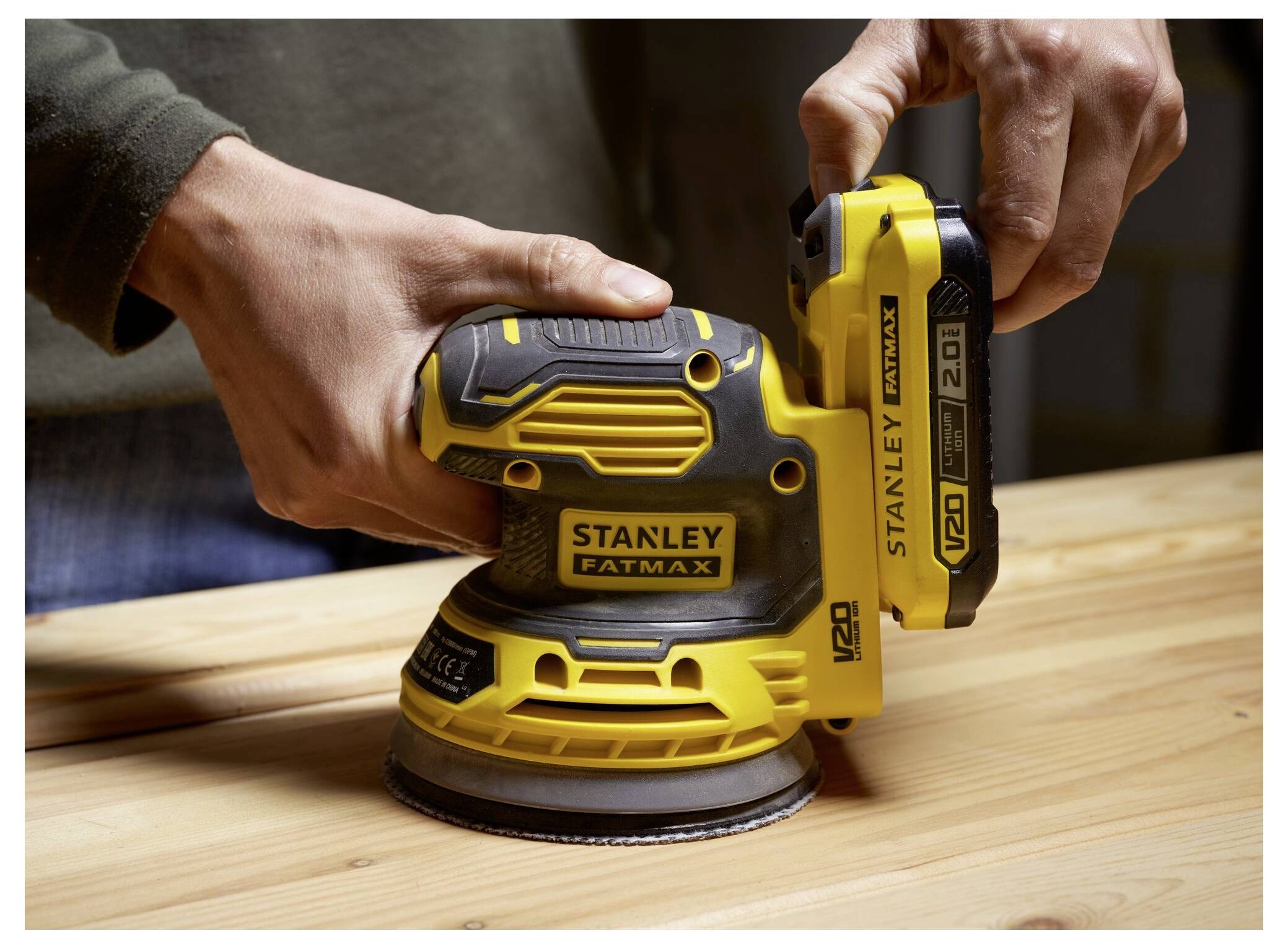 Osoba používající žluto-černý Stanley Fatmax brusku na dřevěné ploše, zdůrazňující detail nářadí a práci se dřevem.