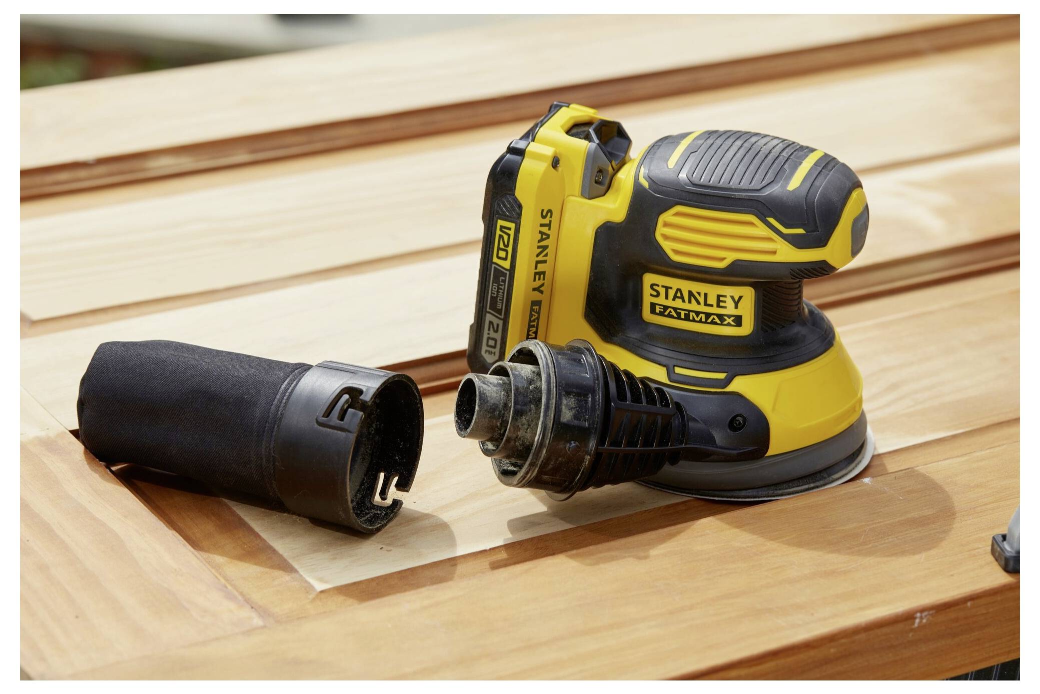 Žluto-černá elektrická bruska spočívá na leštěném dřevěném povrchu, vedle ní je umístěna příprava pro sběr prachu.