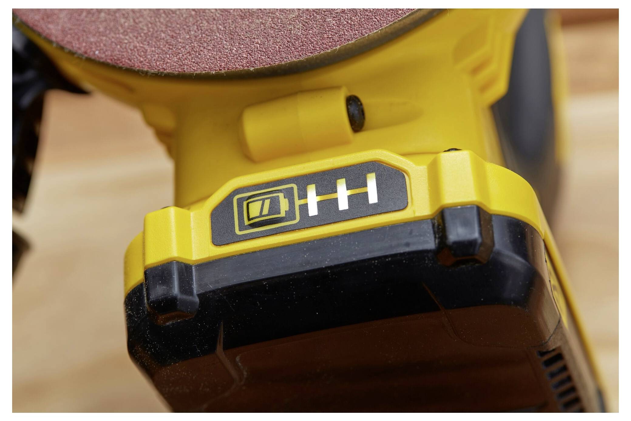 Detailní pohled na žlutou baterii elektrickéího nářadí se třemi indikátory nabití, která je zcela nabitá.