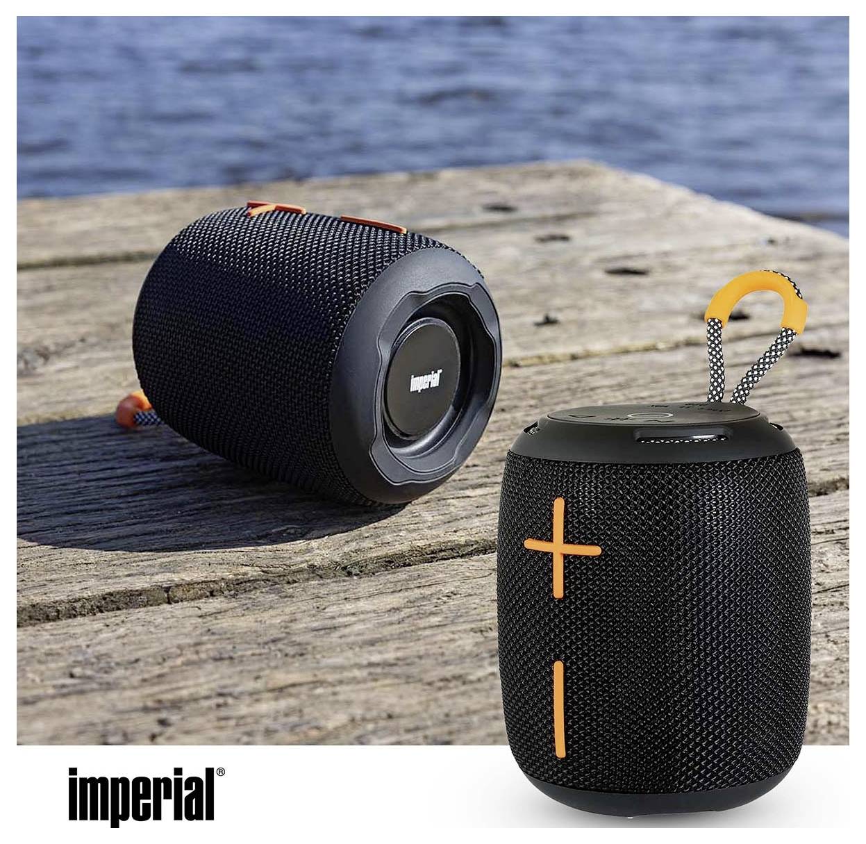 Přenosný Bluetooth reproduktor na dřevěném povrchu, ukazující ovládání hlasitosti a přepravní pásku, značený jako "imperial".