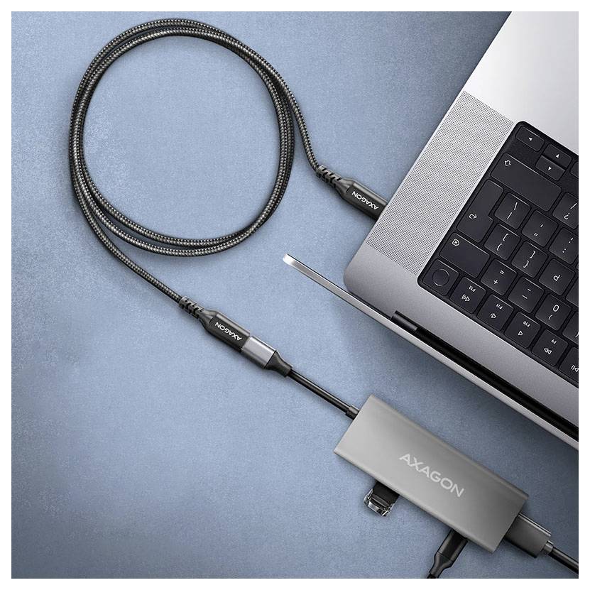 USB-C hub připojený k notebooku pomocí pletencového kabelu, zobrazující adaptér AXAGON na modrém pozadí.