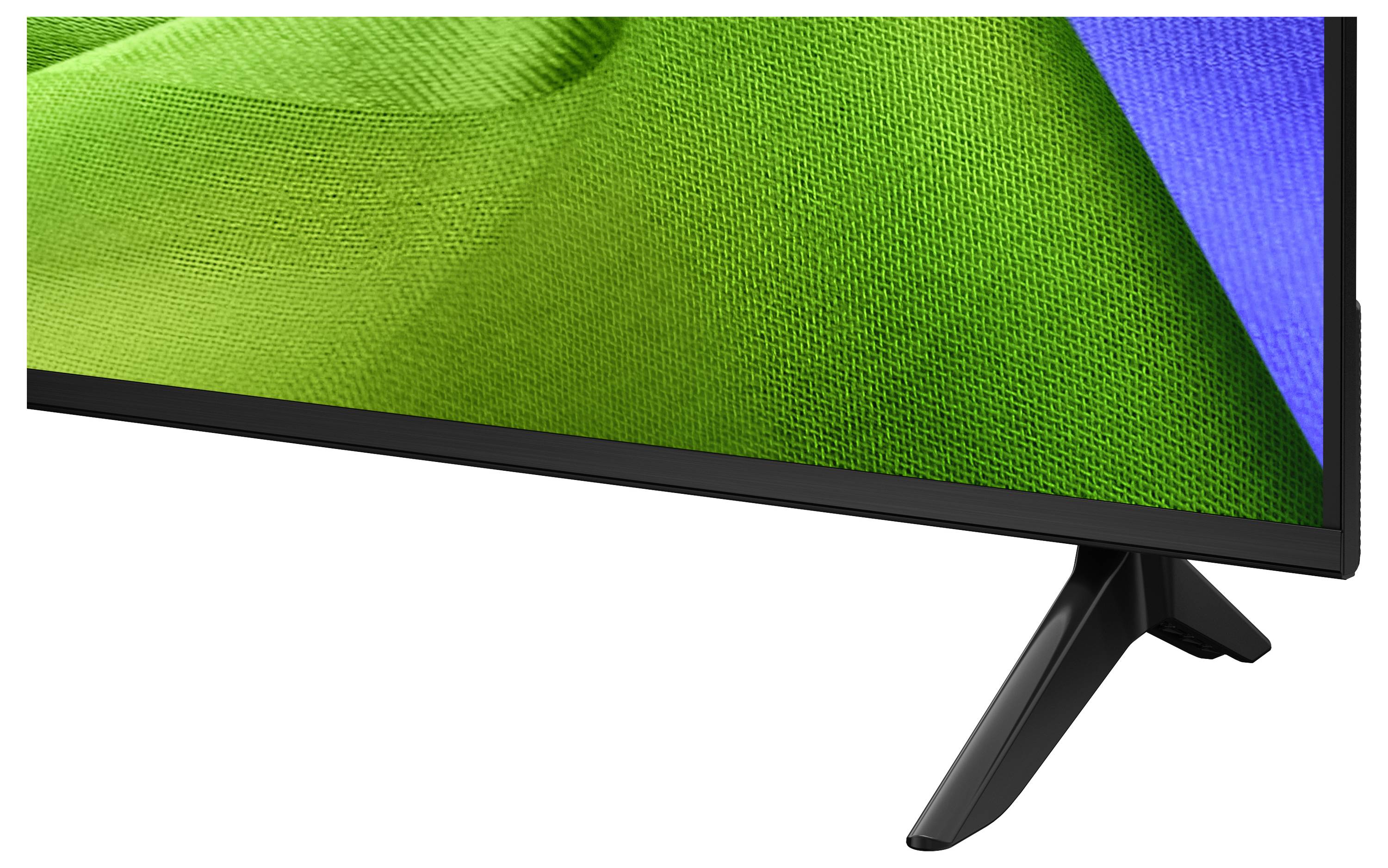 Detailní pohled na plochý televizor nebo monitor se zeleným displejem, černým rámečkem a skloněným stojanem na bílém pozadí.