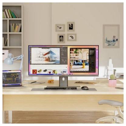 Moderní pracovní stůl s velkým monitorem zobrazujícím designový software, laptop, klávesnice, myš a lampou v jasné domácí kanceláři.
