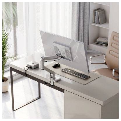 Moderní domácí kancelář s velkým monitorem na kloubovém rameni, klávesnicí a myší na minimalistickém stole vedle okna a regálu.