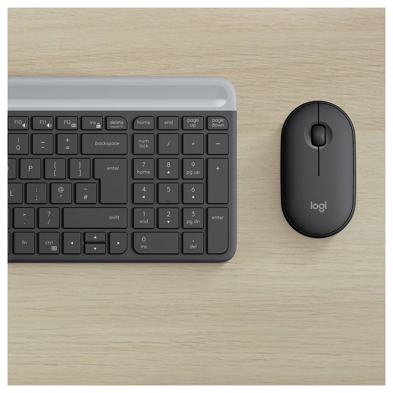 Pohled shora na černou bezdrátovou klávesnici a černou myš Logitech na lehké dřevěné pracovní desce.