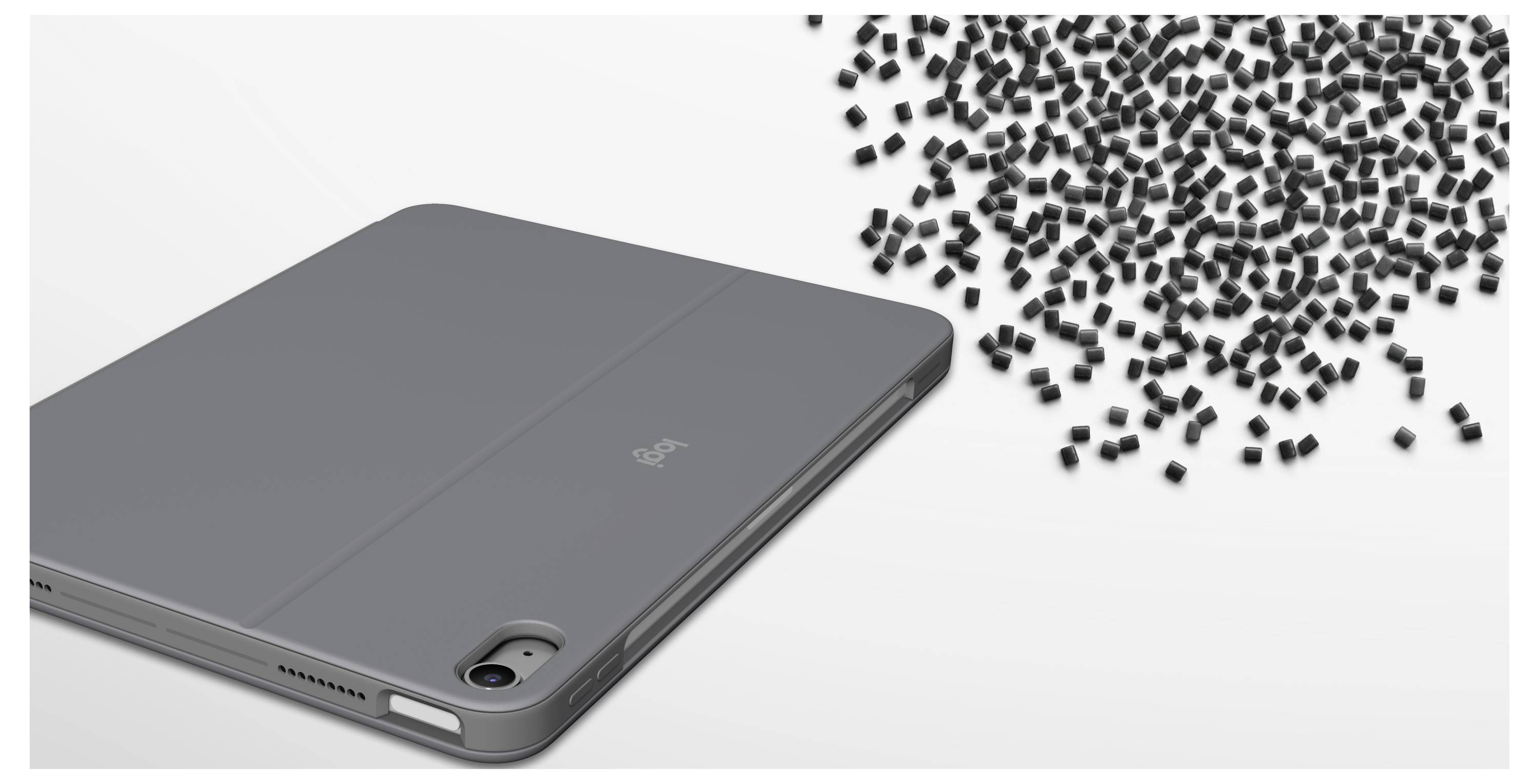 Šedý obal na tablet s vestavěným výřezem pro zadní fotoaparát, zobrazený vedle rozptýlených černých kláves klávesnice na bílém pozadí.