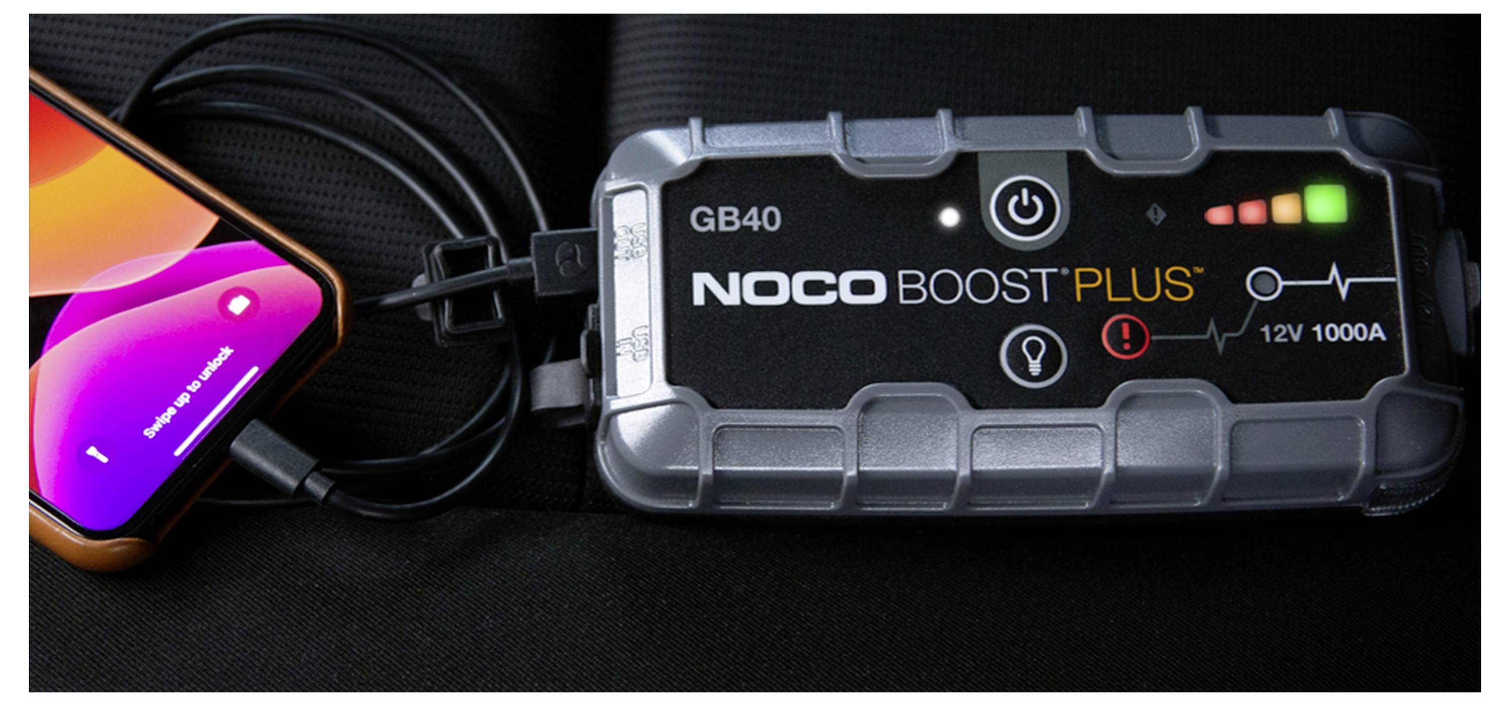 Přenosný startovací booster NOCO Boost Plus GB40 připojený kabelem ke smartphonu se svítícími kontrolkami napájení.