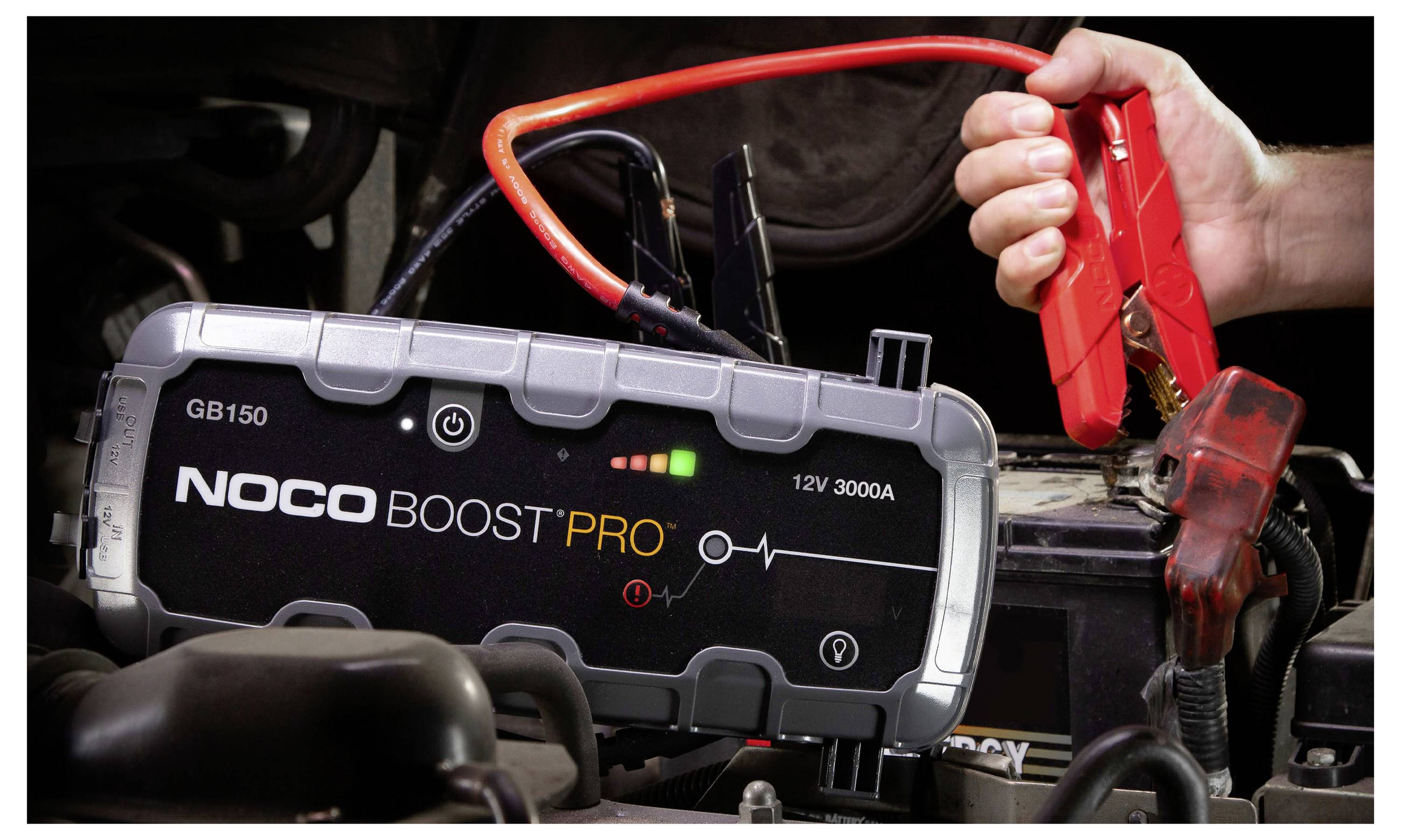 Přenosný startovací zařízení NOCO Boost Pro připojené k autobaterii s červenými svorkami, používané k nastartování vozidla