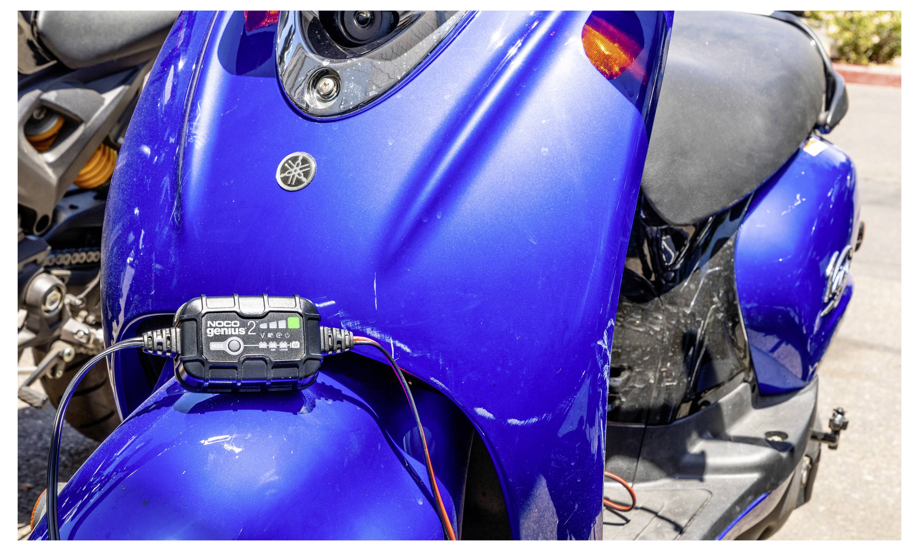 Detailní snímek modrého skútru Yamaha s digitálním zařízením namontovaným na přední části, zobrazující vodiče spojené poblíž řídítek.