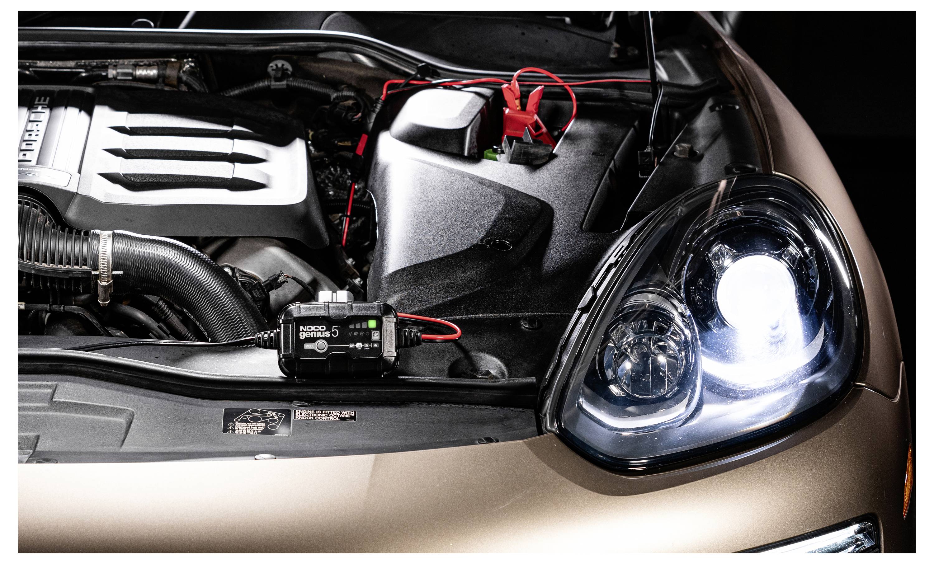 Motorový prostor auta s kabely startovacího kabelu/svorek připojenými blízko reflektoru, což naznačuje nastavení pro spuštění pomocí přenosu energie nebo nabíjení baterie.
