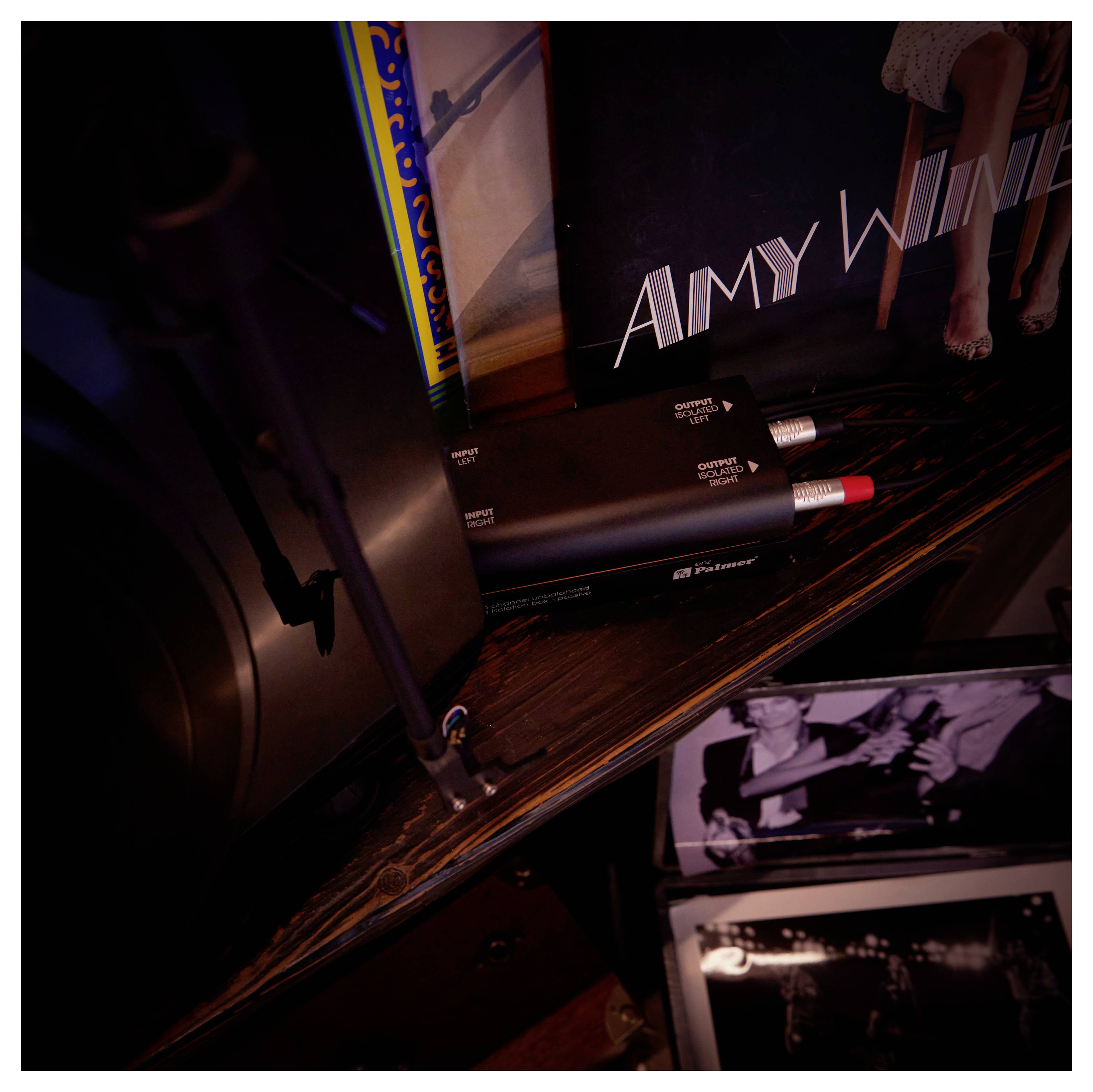 Detailní záběr na Amy Winehouse vinylové sbírky s obalem desky, albuomovým obalem a černočerveným audiotechnikou na polici.