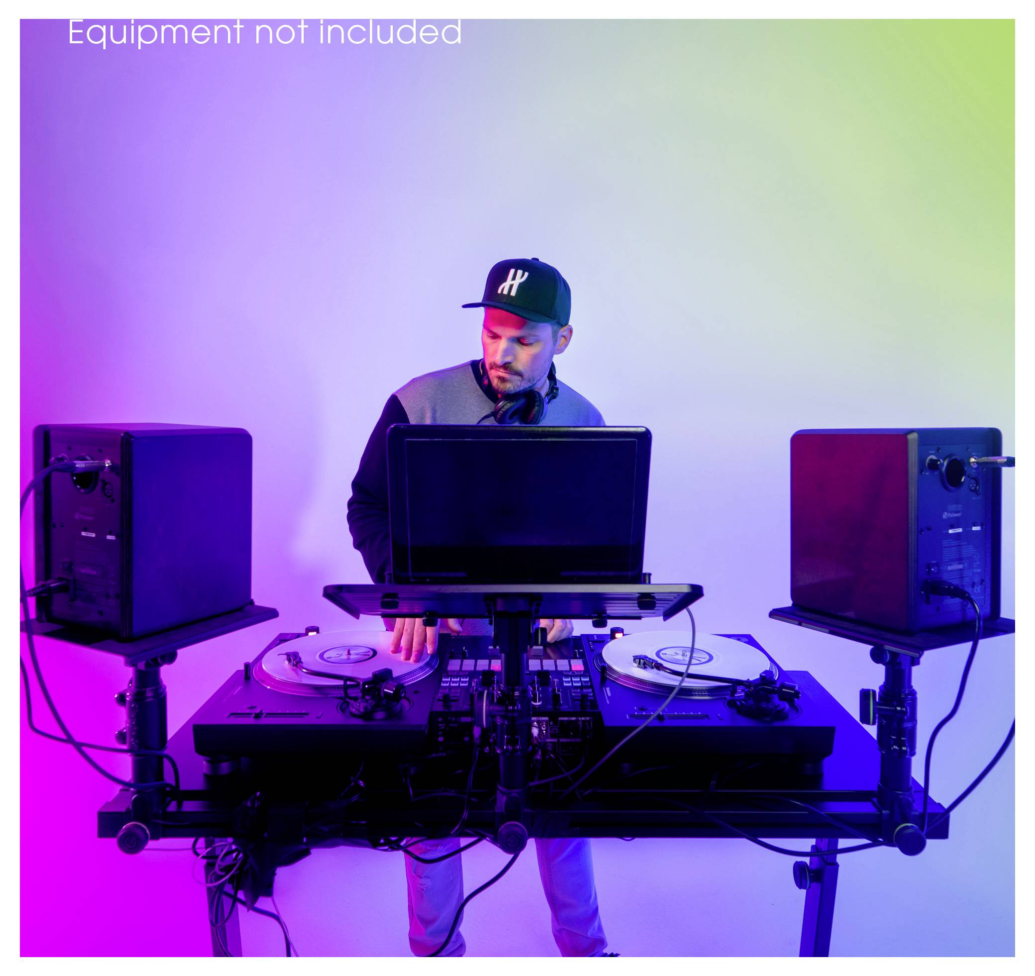 DJ provádějící na dvojitých gramofónech a mixéru za notebookem, obklopen reproduktory, v purpurově-modravém osvětlení.