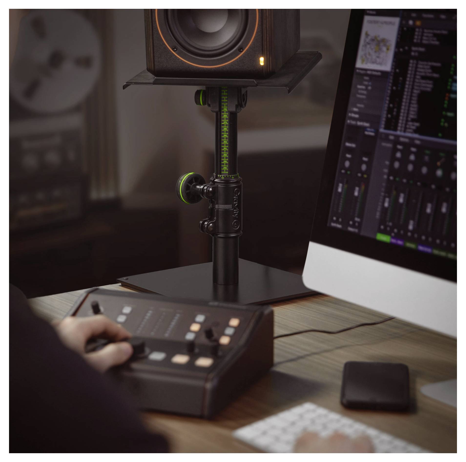 Nastavení audio nahrávání se studiovou monitorovací reproduktorem na nastavitelném stojanu, počítačem s software pro míchání zvuku a osobou ovládající kontrolní panel na pracovním stole.