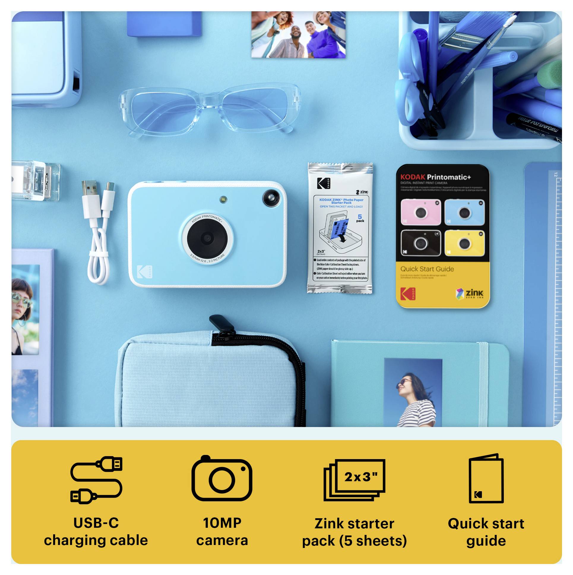 Fotografie z ptačí perspektivy sady Kodak instantního fotoaparátu na modrém pozadí, zobrazující fotoaparát, kabel USB-C, brýle, startovací balíček Zink, příručku rychlého startu a přenosný obal.