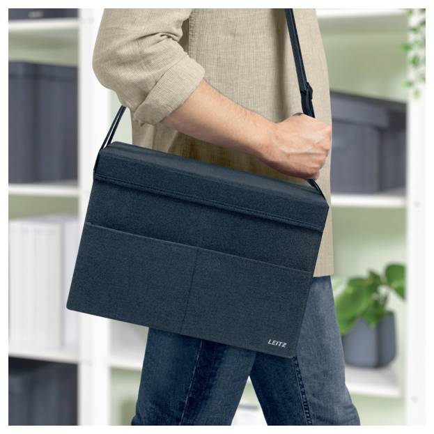 Osoba nošící tmavou crossbody tašku přes rameno nebo pouzdro na notebook v kancelářském nebo domácím prostředí.