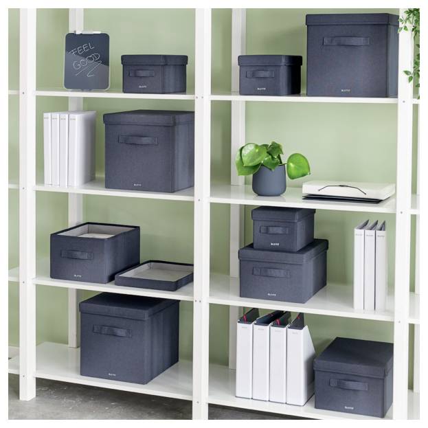 Bílá polička organizovaná s tmavě modrými úložnými krabicemi, bílými pořadači, rostlinou a deskou se zprávou "CÍTIT SE BEN" na pozadí světle zelené stěny.