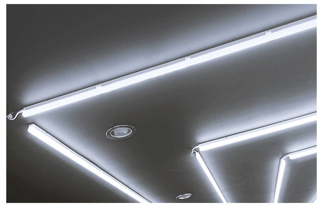 Strop s jasnými geometrickými LED pásky a zapuštěnými svítidly na tmavém povrchu.