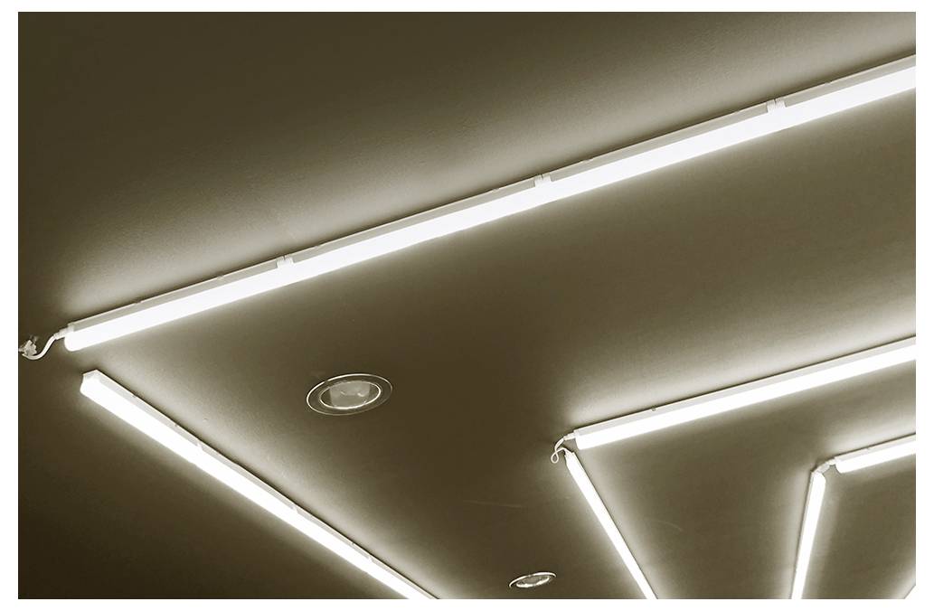 Strop s jasnými geometrickými pásy LED osvětlení a vestavěnými reflektory v moderním interiéru.