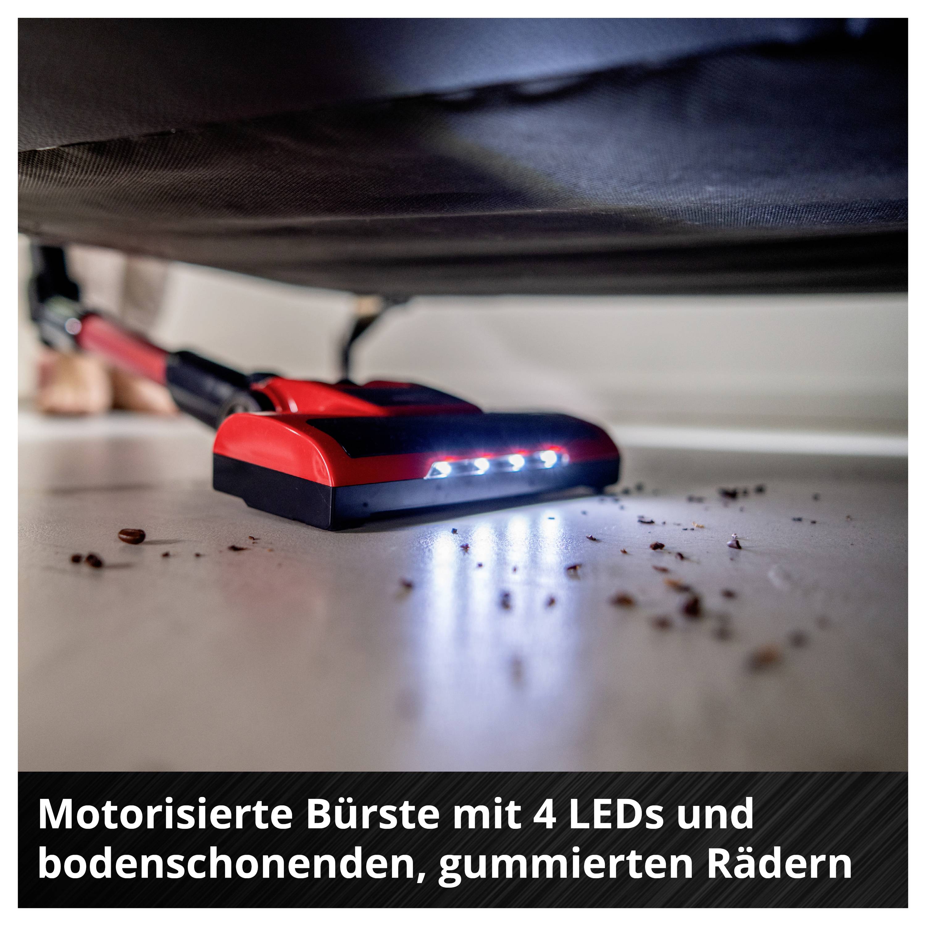 Motorized brush with 4 LEDs and rubber, floor-friendly wheels underneath a piece of furniture, for cleaning hard-to-reach areas.