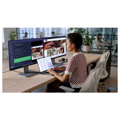 Žena pracující u stolu se dvěma monitory a notebookem v moderní kanceláři, kontrolující kód a rozložení designu.