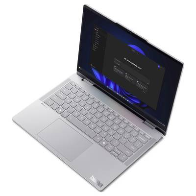 Stříbrný Lenovo laptop s otevřenou obrazovkou zobrazující tmavé rozhraní nastavení/nastavení na modrém ploše ve stylu Windows.
