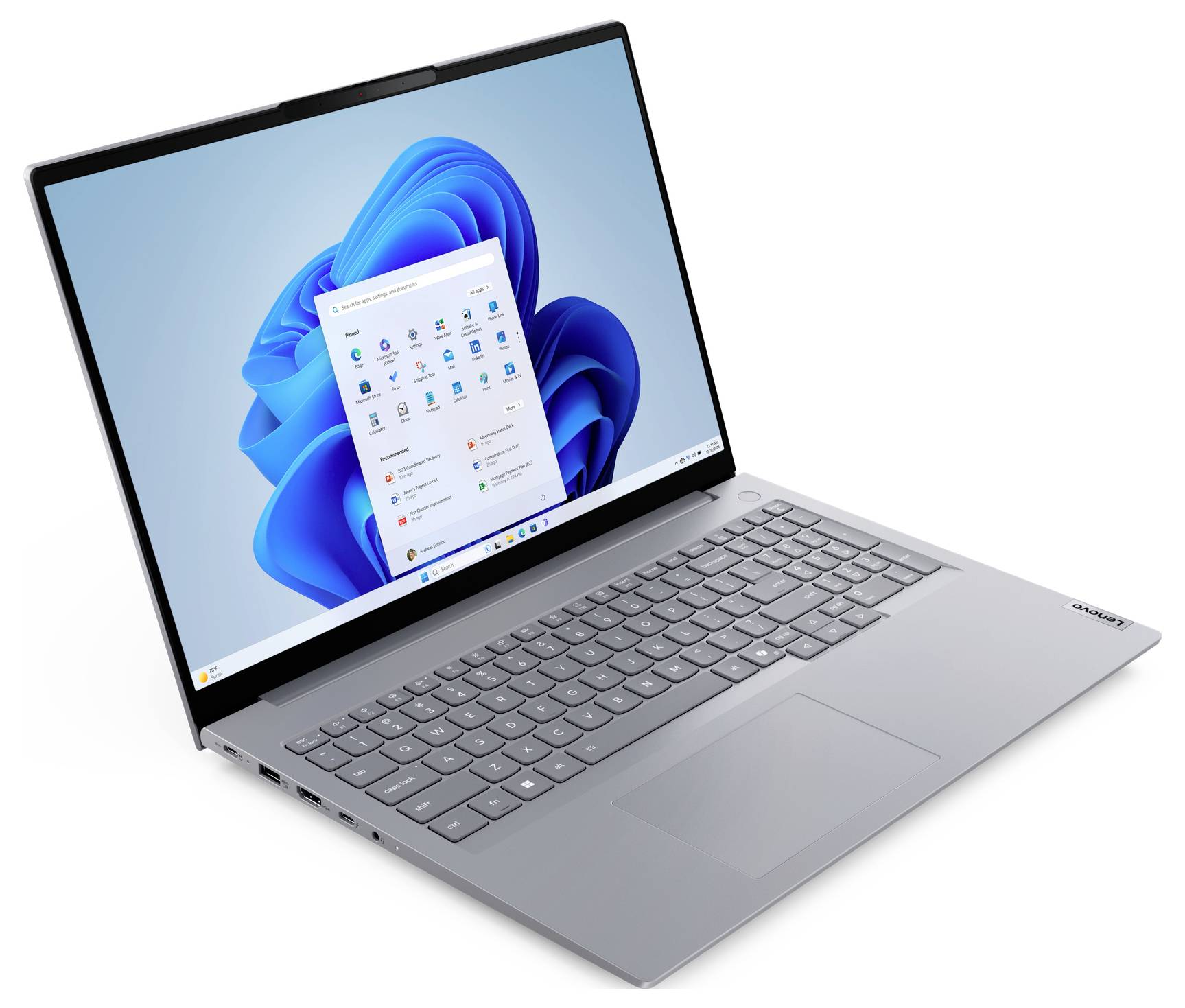 Stříbrný laptop Lenovo otevřený v úhlu, zobrazující plochu Windows 11 a nabídku Start na obrazovce.