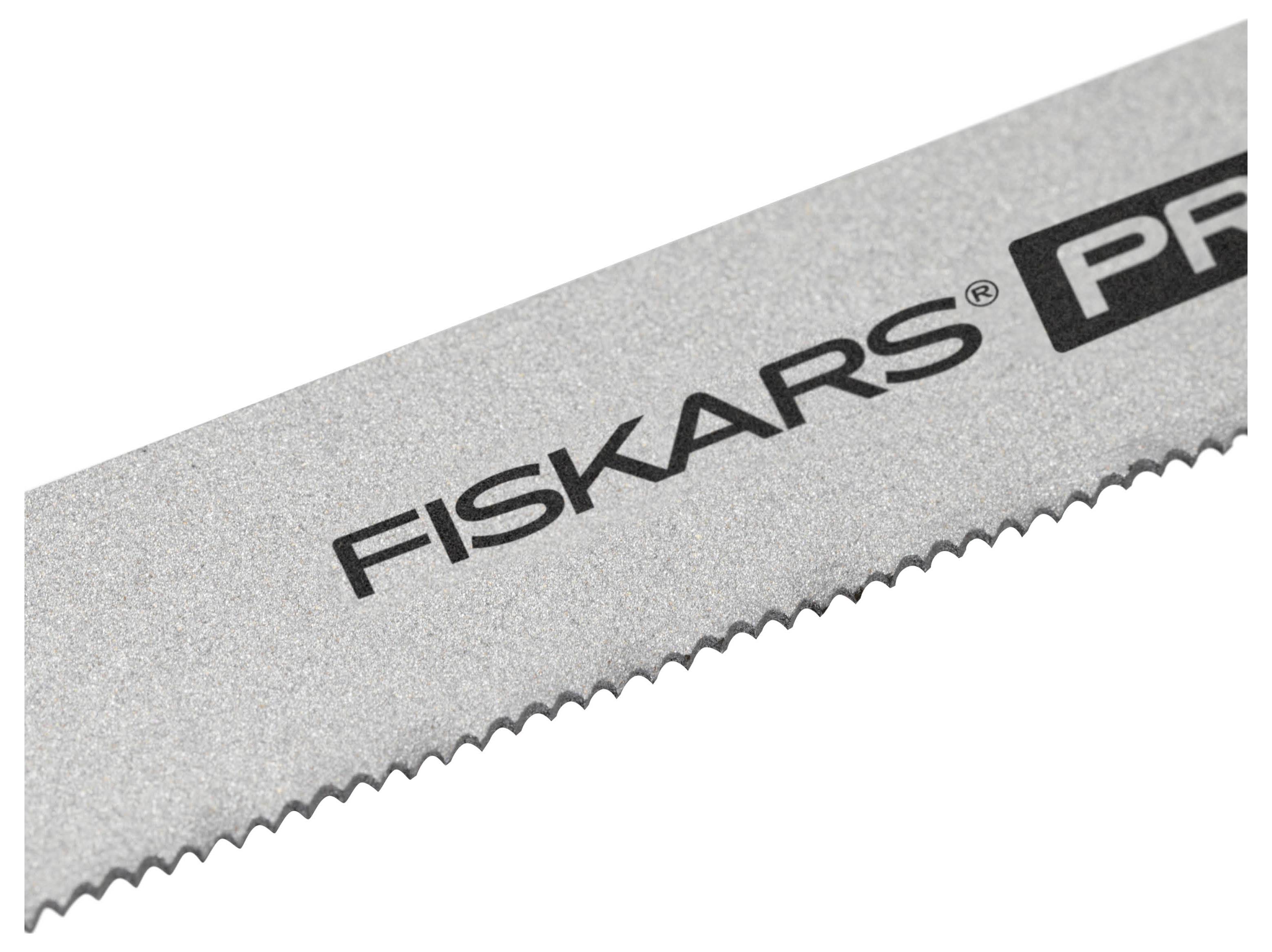 Detailní snímek stříbrného pilového listu Fiskars s jemnými vroubkovanými zuby, zobrazený diagonálně na bílém pozadí.
