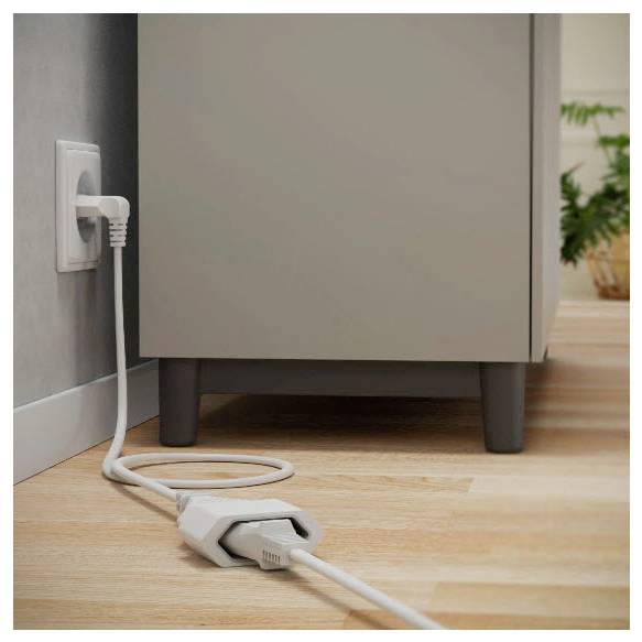 Elektrický kabel zapojený do zásuvky na zdi na podlaze s kabelem svinutým před skříní, ukazující domácí připojení energie.