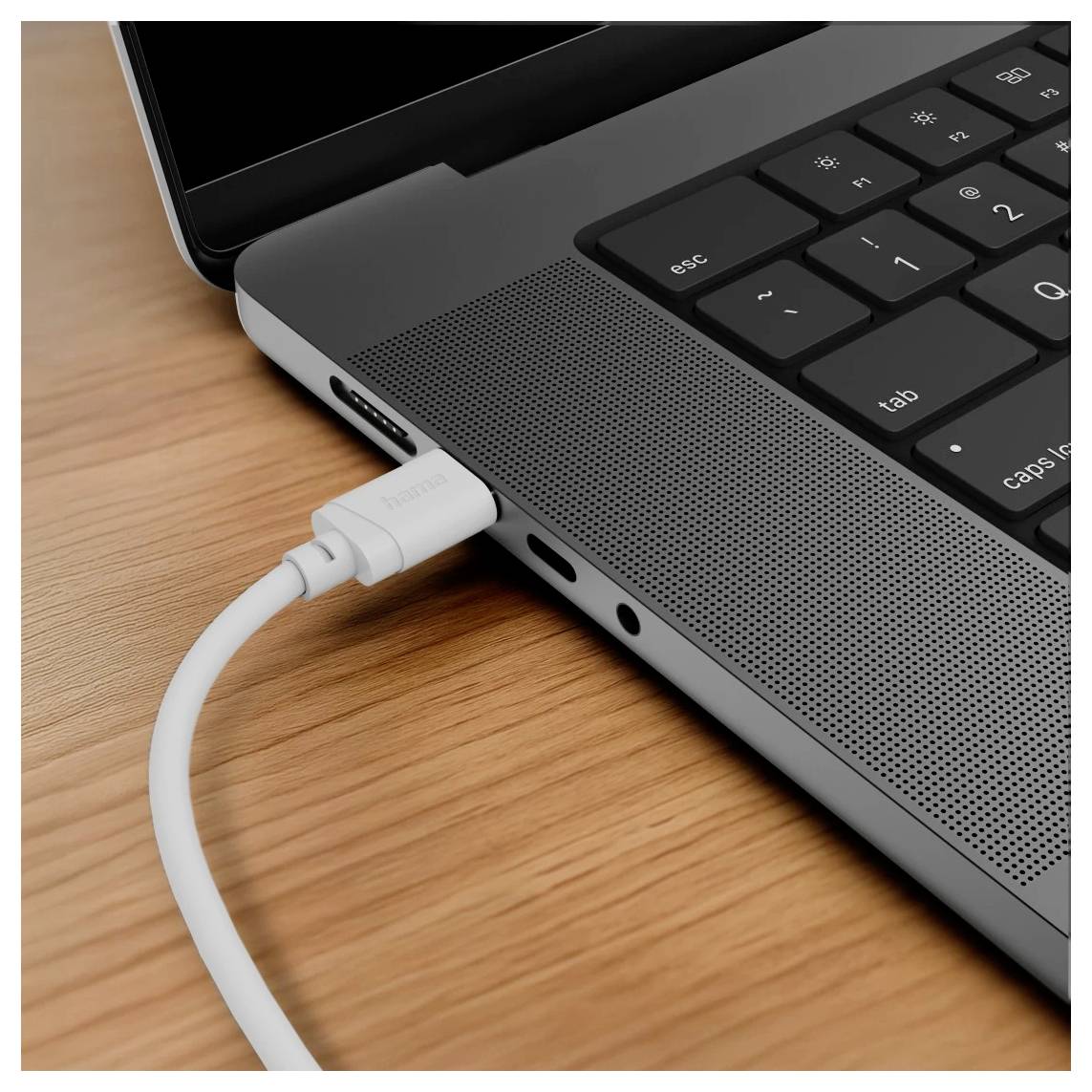 Detailní snímek přenosného počítače s bílým kabelem USB-C zapojeným do bočního portu na dřevěném stole.