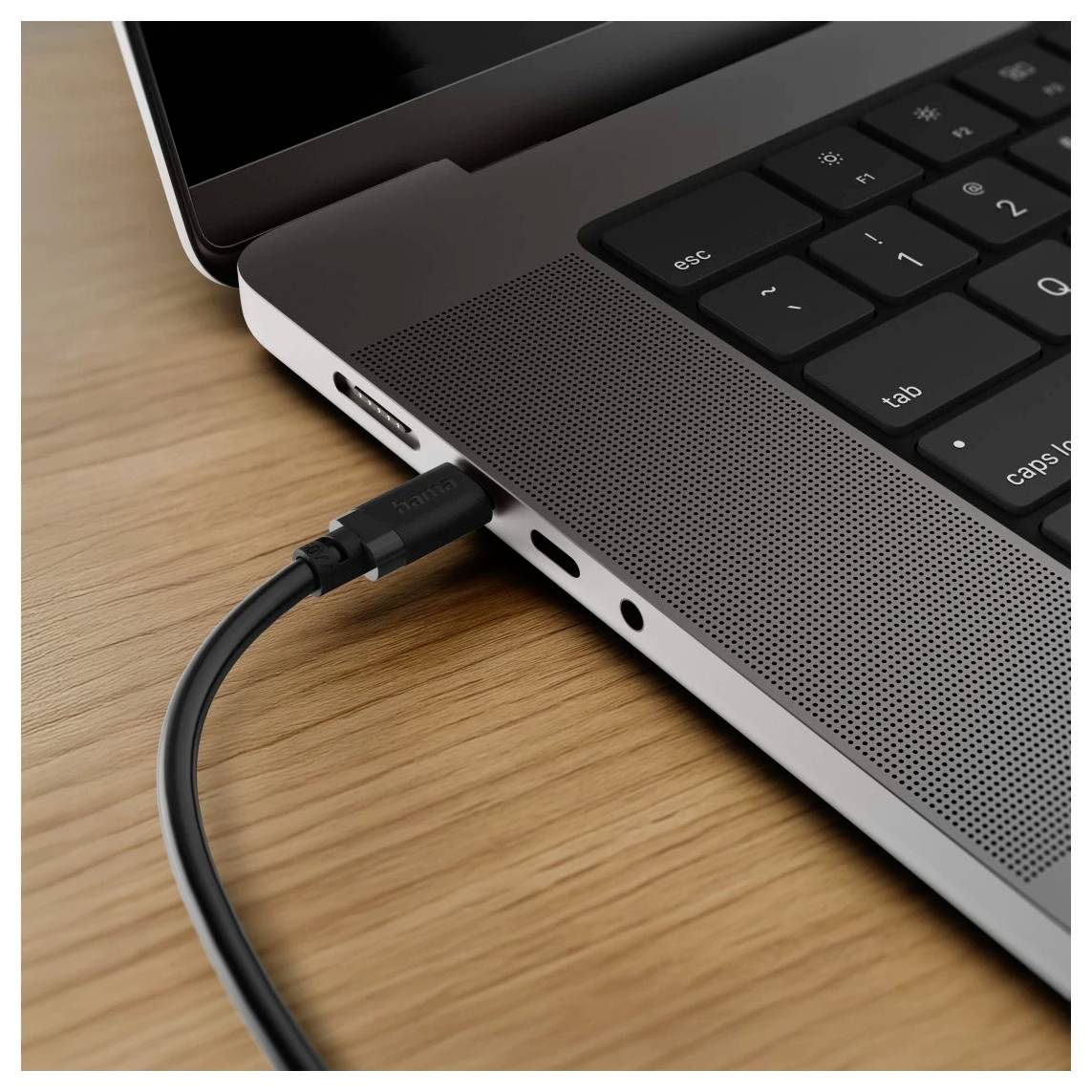 Kabel USB-C zapojený do strany notebooku na dřevěném stole.